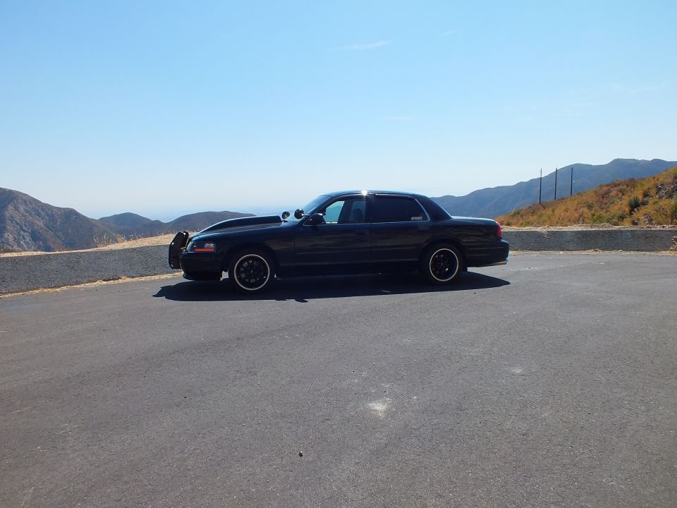 Black Mercury Grand Marquis sedan parked on hilltop road, black wheels