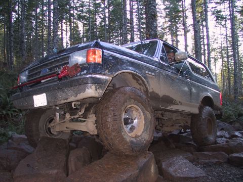 1991 Ford Bronco - A black Ford Bronco navigates a rocky trail in a forest.