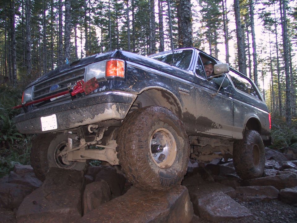 Black Ford Bronco with large tires on rocks, driver visible