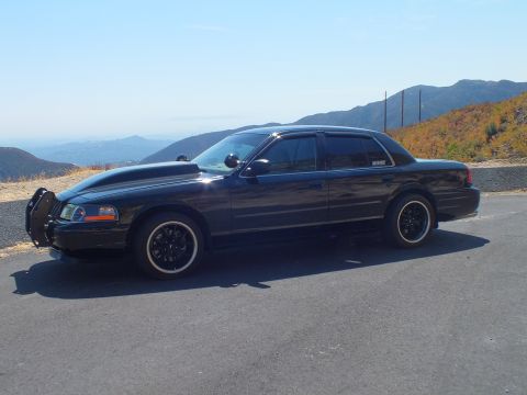 2003 Ford Crown Victoria - Three-quarter view of a black Mercury Grand Marquis with push bar against canyon hills.