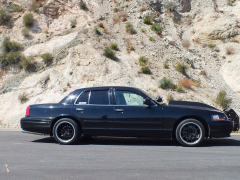2003 Ford Crown Victoria - Profile of a blacked-out Mercury sedan showing the MERCURY emblem on the rear door.