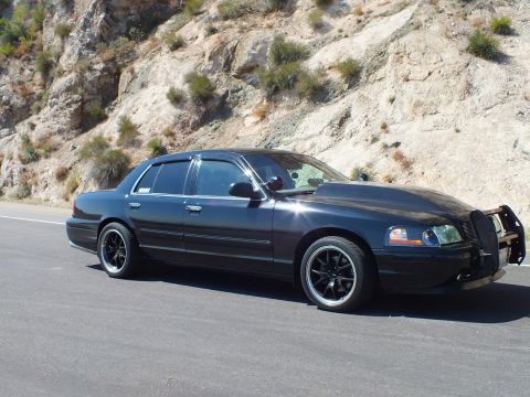 2003 Ford Crown Victoria - Front three-quarter of a black Mercury Grand Marquis with push bar against a road cut.