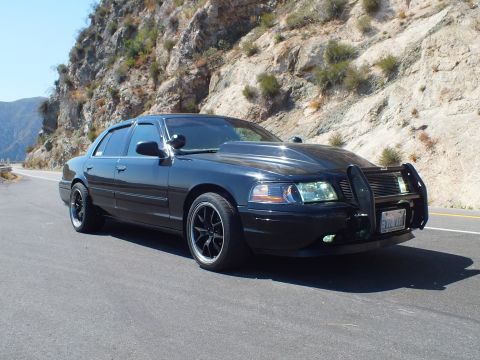 2003 Ford Crown Victoria - Blacked-out Mercury Grand Marquis seen front-on with grille guard, mountain highway behind.