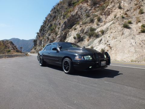 2003 Ford Crown Victoria - Front-quarter view of a black Mercury sedan with push bar parked along a canyon road.