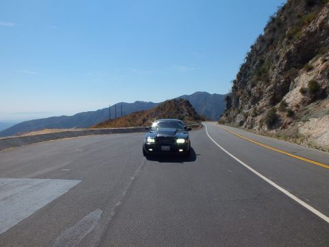 2003 Ford Crown Victoria - Black Mercury sedan approaches head-on along a winding ridgeline highway, lights lit.