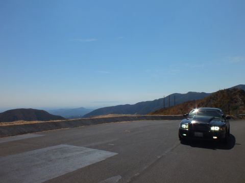 2003 Ford Crown Victoria - Black Mercury sedan parked at a high turnout overlooking layered ranges, headlights on.