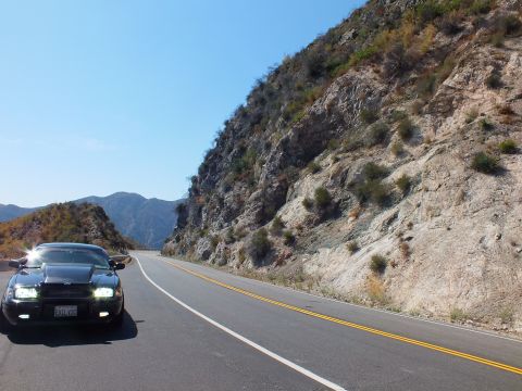 2003 Ford Crown Victoria - Front-quarter view of a black Mercury along a two-lane canyon road by a steep rock face.