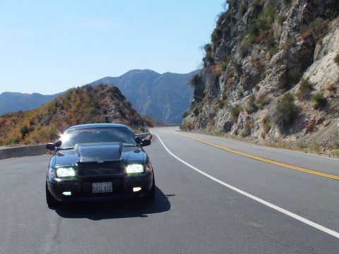 2003 Ford Crown Victoria - Head-on Mercury Grand Marquis with hood scoop and EVIL VIC plate beside a rock cut.