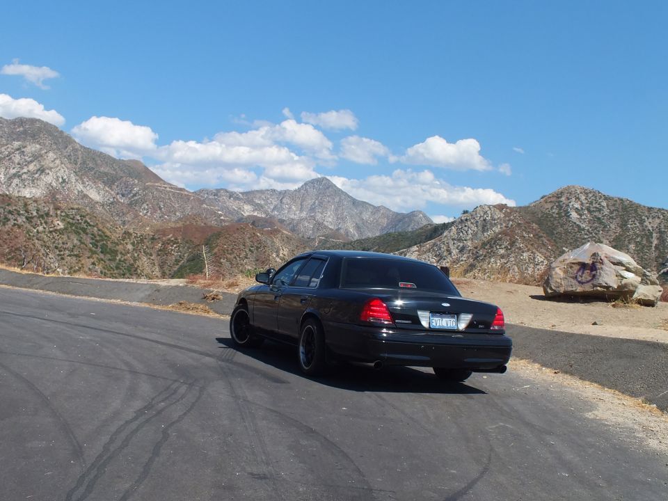 Black Mercury sedan rear-quarter at mountain turnout under blue sky