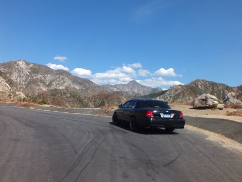 2003 Ford Crown Victoria - Black Mercury Grand Marquis seen from the rear at a turnout below jagged ranges.