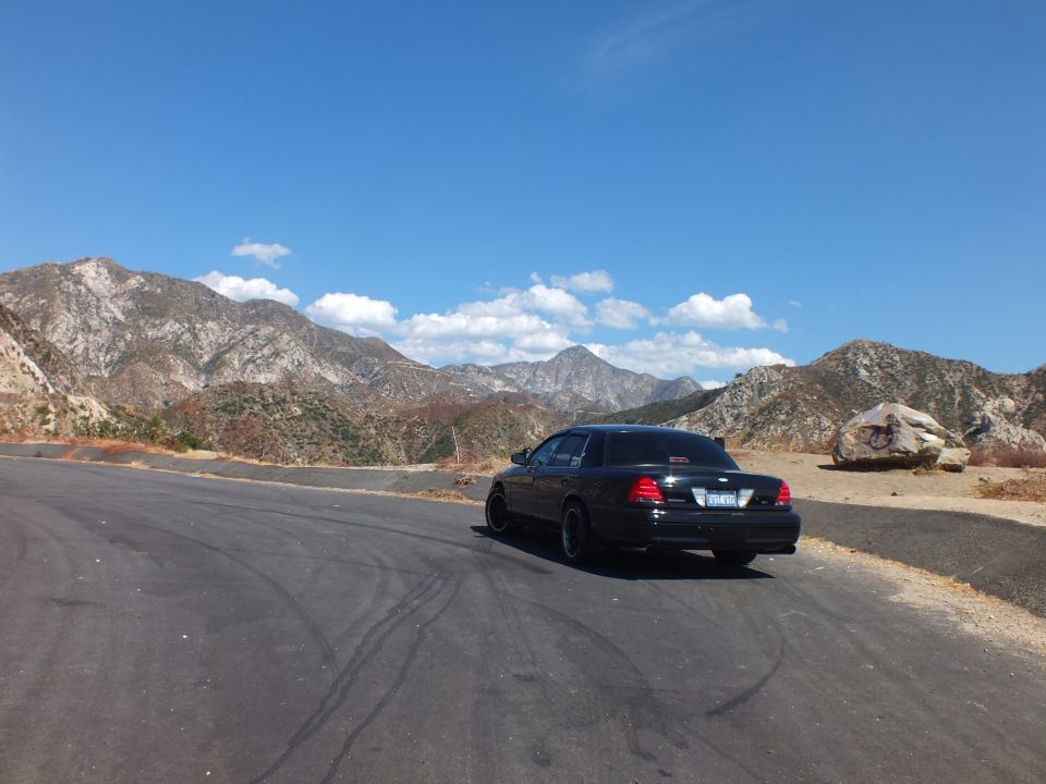 Black Mercury sedan rear view at hilltop pullout with mountain panorama