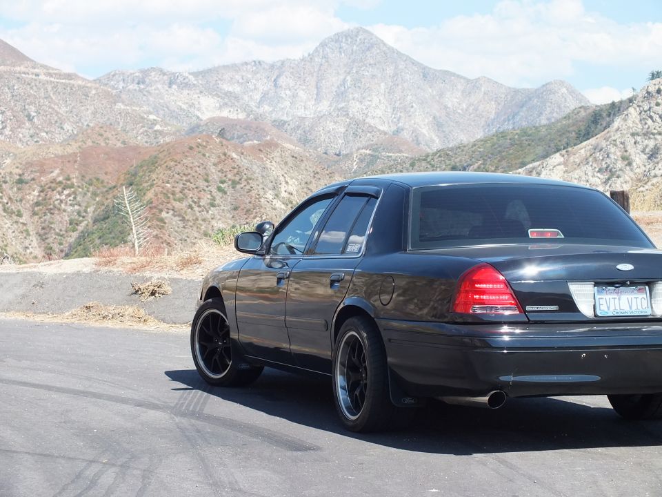 Black Mercury sedan rear-quarter with Mercury emblem and EVIL VIC plate, mountains