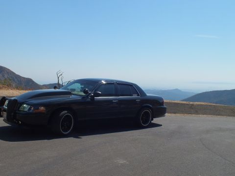 2003 Ford Crown Victoria - Profile of a lowered black Mercury sedan parked at a high turnout above hazy ranges.
