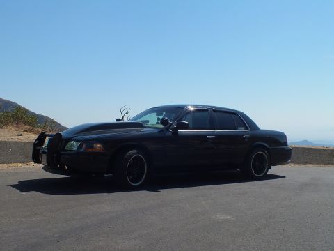 2003 Ford Crown Victoria - Murdered-out Crown Vic with push bar sits at a hilltop turnout under clear sky.