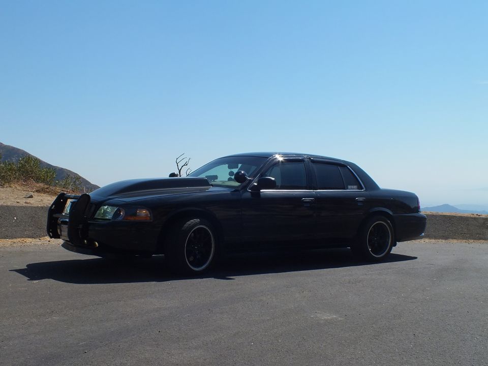Black Ford Crown Victoria sedan parked at mountain pullout, side profile on black wheels