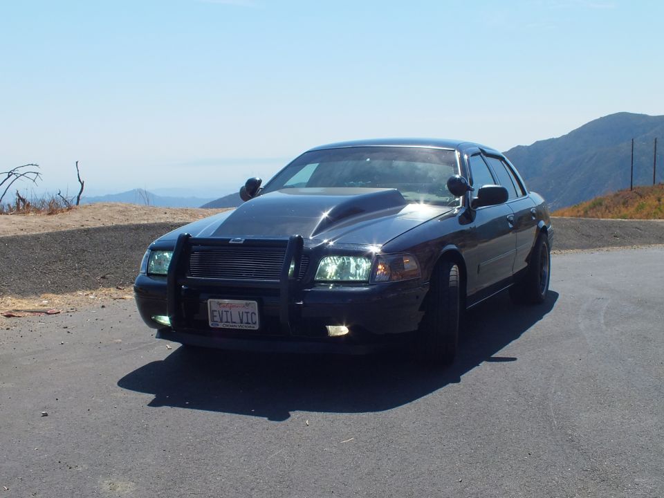 Black Ford Crown Victoria front quarter with push bar, EVIL VIC plate, mountains behind