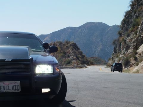2003 Ford Crown Victoria - Close front-corner view of a Crown Vic; a dark SUV waits down the curving canyon road.