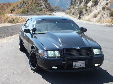 2003 Ford Crown Victoria - Crown Vic front-quarter at a turnout; a rider passes on the canyon road beyond.