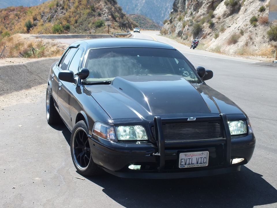 Black Ford Crown Victoria front three-quarter with grille guard, motorcycle on road behind
