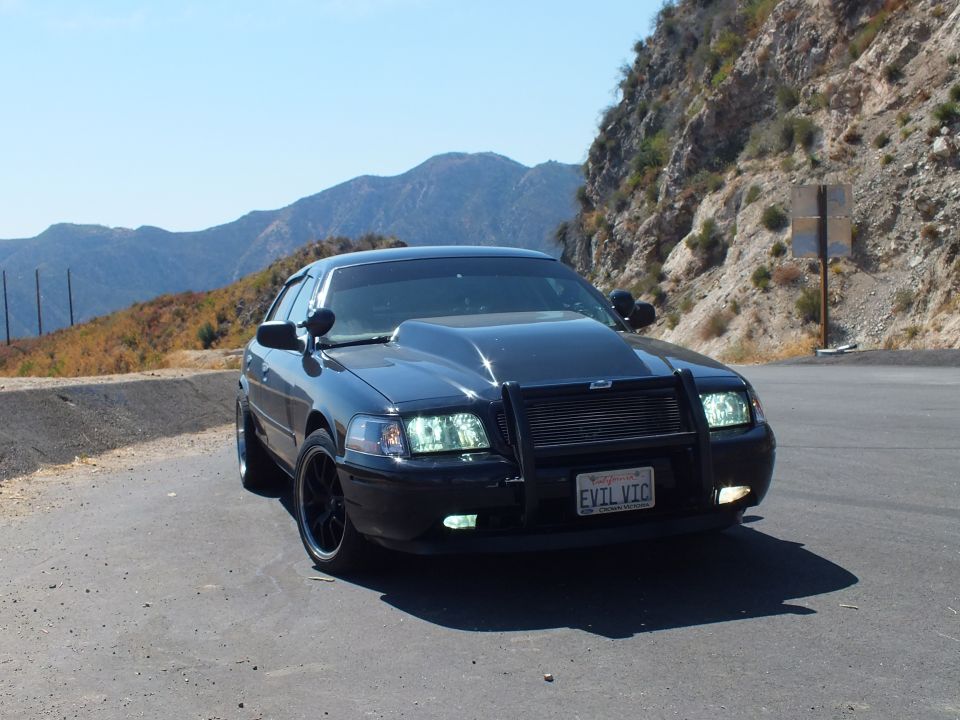 Black Ford Crown Victoria front quarter with grille guard, mountains and road behind
