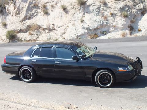 2003 Ford Crown Victoria - Side profile of a lowered Crown Vic with tinted glass against a rocky slope.