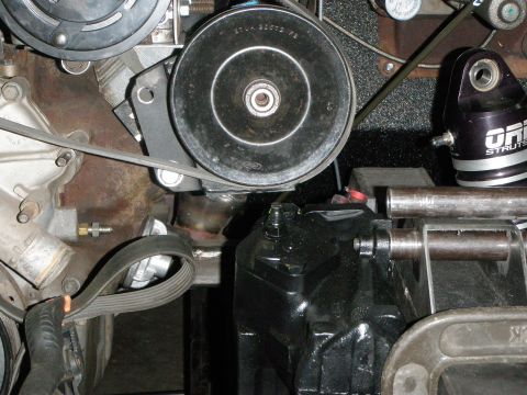 1961 International Scout 800 - Detail view of engine components and steering system, including a pulley and a black steering gear box.