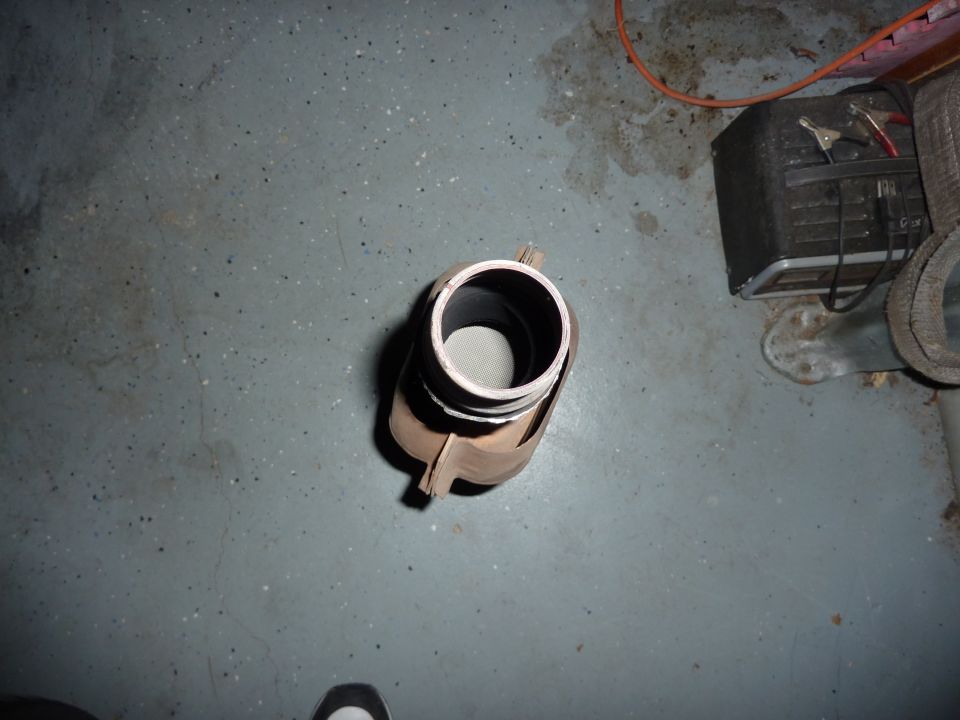 Exhaust pipe part on a gray concrete floor, with a battery charger and orange cord in the background