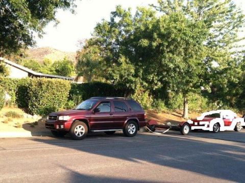 1995 Ford Probe - A red SUV tows a red and white car down a tree-lined street, with a house visible in the background.