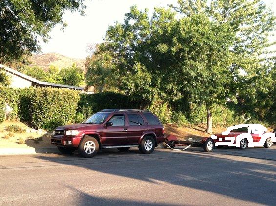 Red SUV towing a red and white car on a residential street