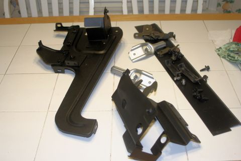 1976 Ford Ranchero - Several black metal automotive components and hardware are arranged on a tiled surface.