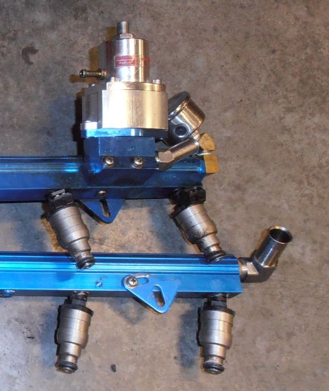 1990 Ford Bronco - A close-up view of a fuel injector rail assembly, including the regulator and injectors.