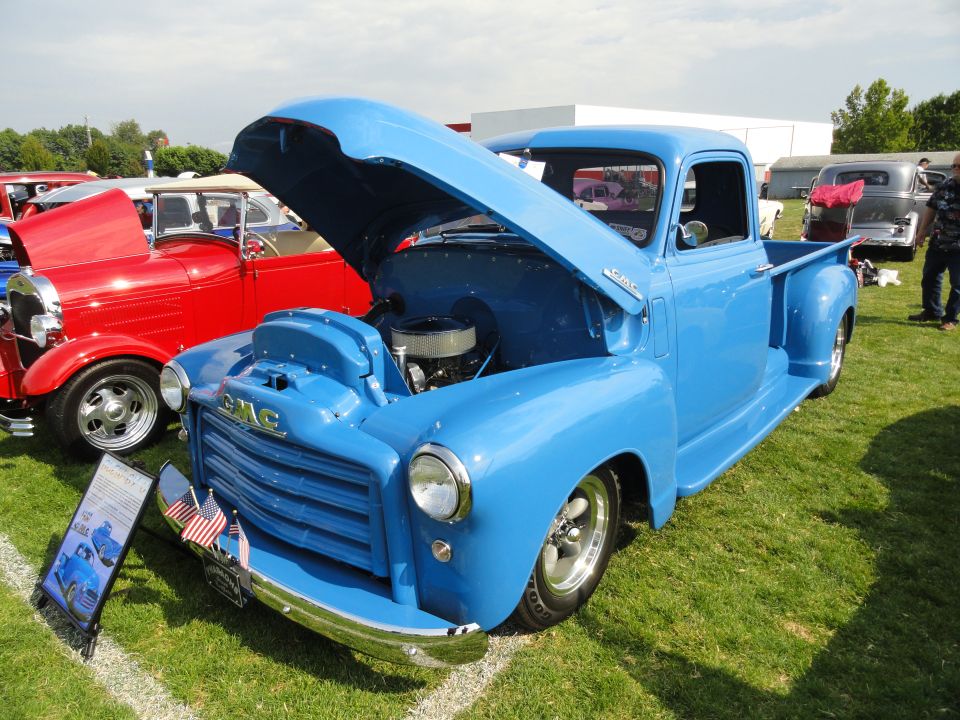 Blue 1950s GMC pickup truck with hood open, chrome grille, and custom wheels parked on grass