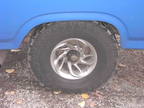 1980 Ford Bronco - Close-up of a blue vehicle's wheel and fender, an off-road tire and chrome rim.