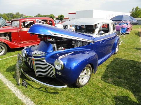 1964 Ford Fairlane - A blue sedan with its hood open is displayed at a car show, parked next to a red vehicle.