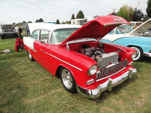 1964 Ford Fairlane - A red and white 1955 Chevrolet sedan is displayed with its hood open at a car show, alongside other vehicles.