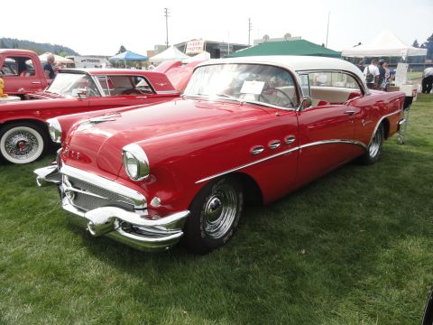 1964 Ford Fairlane - A classic red and white Buick is displayed at a car show, parked next to another vehicle.