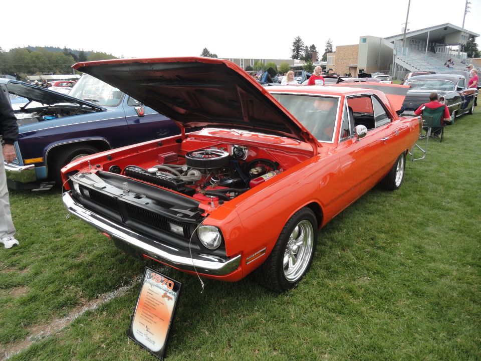 Orange 1968 Dodge Dart with hood open, parked on grass next to a blue pickup truck