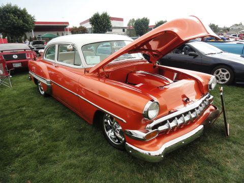 1964 Ford Fairlane - A classic orange and white sedan is displayed with its hood open at an outdoor car show.