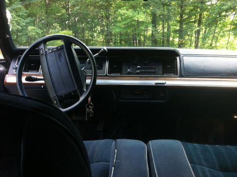 1991 Ford LTD Crown Victoria - The interior of a car is shown, with a view of the dashboard and seats, set against a backdrop of trees.