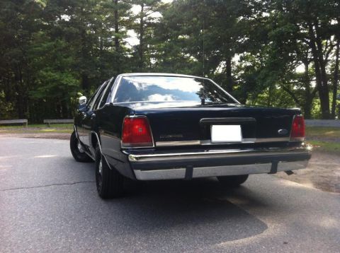 1991 Ford LTD Crown Victoria - Rear view of a dark 1991 Ford Crown Victoria LTD sedan parked on a road with trees in the background.