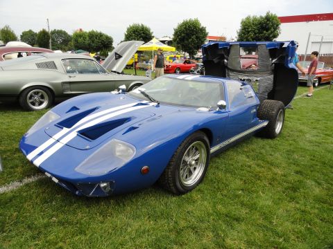 1964 Ford Fairlane - A blue Ford GT40 with white racing stripes is displayed at a car show, its rear engine cover lifted.