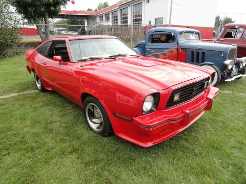 1964 Ford Fairlane - A red coupe with flame graphics sits on the grass at a car show, with other vehicles visible in the background.
