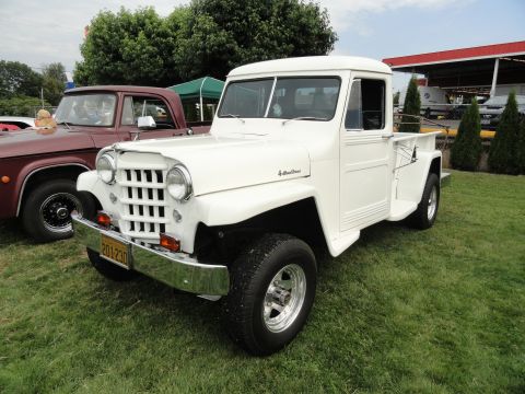 1964 Ford Fairlane - A white Jeep pickup truck is parked on grass next to a maroon pickup truck.