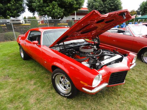 1964 Ford Fairlane - A bright red 1970 Chevrolet Camaro is displayed with its hood open at a car show, revealing the engine bay.