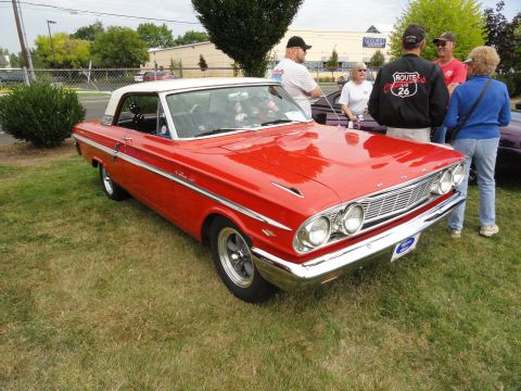 1964 Ford Fairlane - A red 1964 Ford Fairlane with a white roof is displayed at a car show.