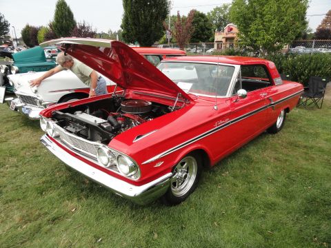 1964 Ford Fairlane - A man looks at the engine of a red 1964 Ford Fairlane at a car show.