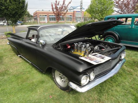 1964 Ford Fairlane - A matte black custom pickup truck from 1959 is displayed with its hood open, revealing a powerful V8 engine.
