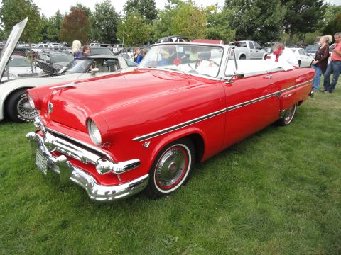 1964 Ford Fairlane - A red 1955 Ford Fairlane convertible is displayed at a car show with other vehicles present.