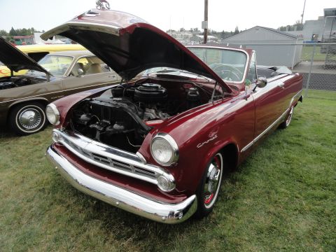 1964 Ford Fairlane - A maroon convertible with its hood open is parked on grass next to another car.