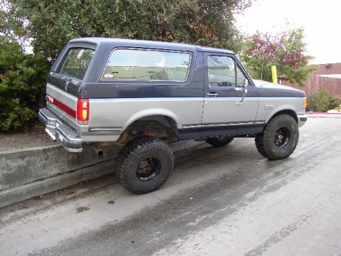 1989 Ford Bronco - This lifted Ford Bronco has a two-tone paint scheme and is parked with its rear wheels on a concrete barrier.